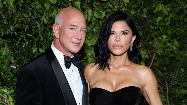 Jeff Bezos in a tuxedo and Lauren Sanchez in a black dress posing in front of green backdrop at the MET Gala