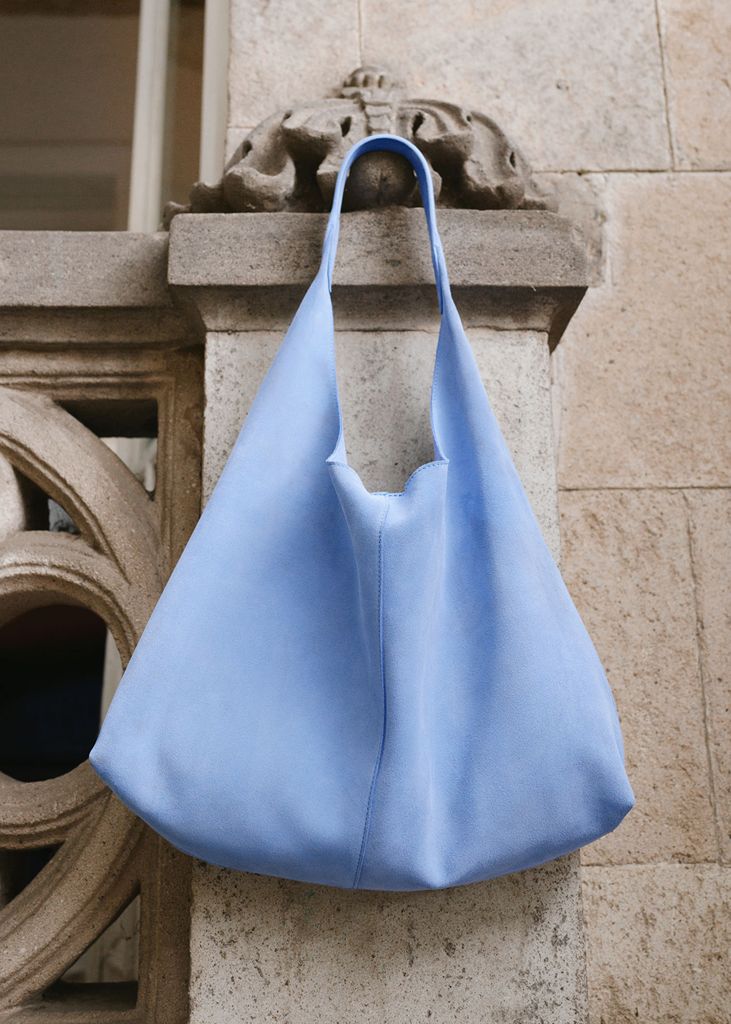 A blue suede tote bag hangs on a concrete pillar 