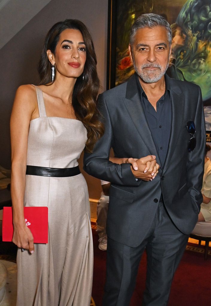 Amal Clooney and George Clooney hold hands while smiling for photographer at event in London