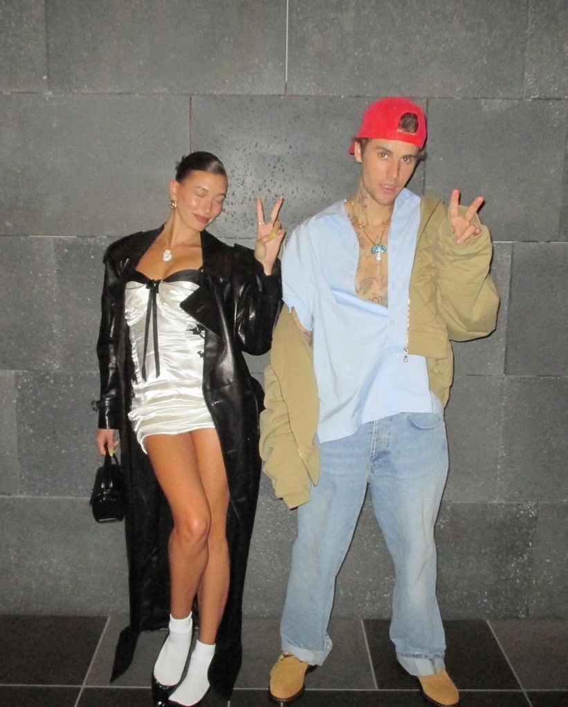 Hailey and Justin Bieber stand in front of brick wall throwing peace signs
