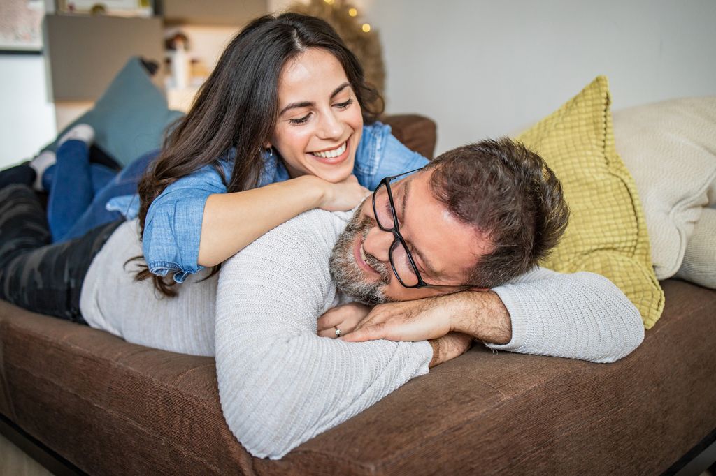 Photo of happy couple relaxing at home. They are laying on the couch and smiling