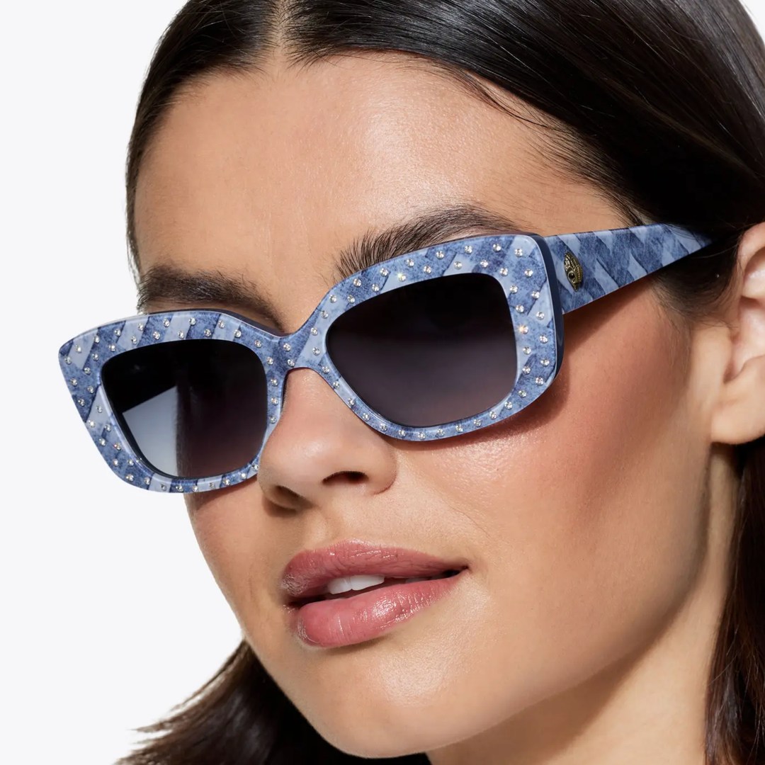 A model with brown hair poses for a close up photo wearing denim toned sunglasses from Kurt Geiger